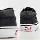 A close-up of two Skate Rowan Asphalt White VN0A5JICRP9 Suede Vans shoes highlights the black suede heel. The white sole displays the red Vans Off The Wall logo on the back, with one shoe in the foreground, slightly out of focus.