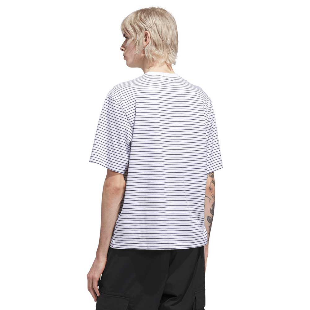 Person with short blond hair, viewed from behind, wearing the Adidas Skateboarding Skate Yarn Dye Tee in White Dark Blue (KC6291), featuring thin dark blue horizontal stripes, paired with black pants. A tattoo is visible on their left arm.