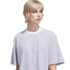 A person with short, blonde hair wears the Skate Yarn Dye Tee White Dark Blue (KC6291) from Adidas Skateboarding, featuring thin black horizontal stripes, and looks slightly to the side against a plain white background.