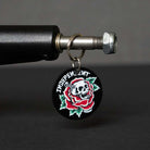 A round keychain with a skull and red rose design featuring Cyrillic text, inspired by the Independent Truck Company, hangs from a metal bolt alongside the Stage 4 Eric Dressen Pro 151 Black Silver Standard INDY Trucks Set of TWO.