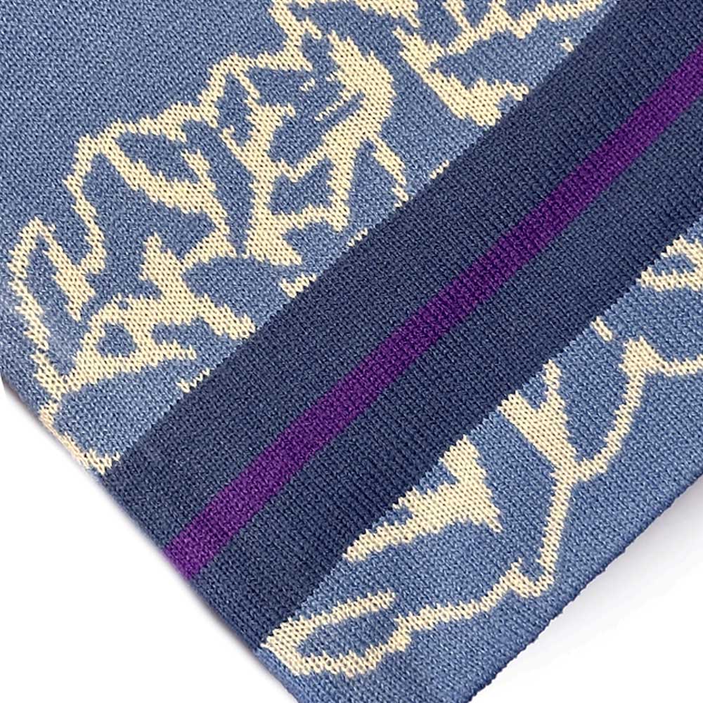 Close-up of the Striped Beanie Blue Late Nite Stars Skateboarding, featuring blue knitted fabric with cream floral patterns and a dark blue border accented by a single purple stripe.