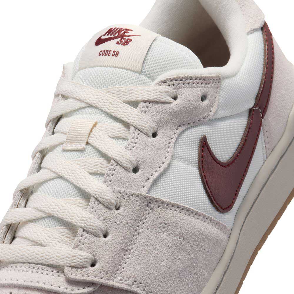 Close-up of a white and grey suede Summit White Mystic Dates Code 58 IB0108102 Nike SB Skateboarding Suede Shoe with a maroon swoosh and CODE 58 printed on the tongue tag.
