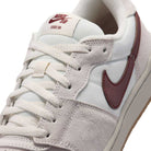 Close-up of a white and grey suede Summit White Mystic Dates Code 58 IB0108102 Nike SB Skateboarding Suede Shoe with a maroon swoosh and CODE 58 printed on the tongue tag.
