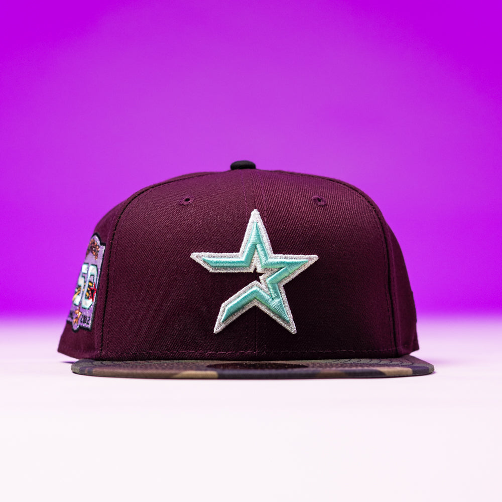 The Swag Era 50th Camo Maroon Houston Astros New Era 5950 Fitted Hat features a maroon design with a teal and white star, a 50th Camo Maroon anniversary side patch, and stands out against a purple gradient background.