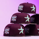 Five Swag Era 50th Camo Maroon Houston Astros New Era Hat 5950 Fitted caps are stacked in a pyramid against a purple gradient background, each featuring a teal star logo and a 50th Anniversary patch.