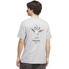 A person wearing the TOS Crane Tee Gray KY7718 from Adidas Skateboarding, which features a graphic of two cranes and stylized text on the back, stands facing away from the camera.