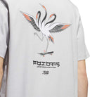 A person wearing the TOS Crane Tee Gray (KY7718) from Adidas Skateboarding—a skateboarding t-shirt featuring an illustration of two cranes on a skateboard with stylized text and signatures below the image, inspired by the Temple of Skate collaboration.
