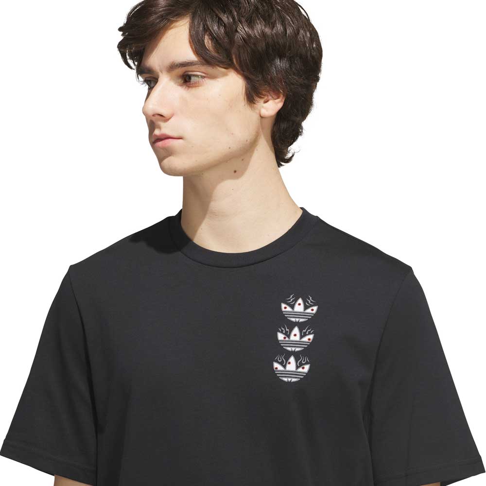 A young person with medium-length brown hair is wearing the TOS Curb Tee Black Multi KS4338 from adidas Skateboarding, a black tee featuring three stacked, multi-colored Adidas trefoil logos on the left chest. They look to their left, effortlessly channeling skate culture style.