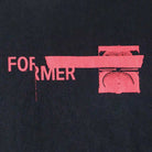 The Tape Crux Former Tee Black features the word FORMER in pink, partially covered by a pink bar beside an abstract pink circular pattern—all set against a black background. This bold design recalls the vintage style and classic screen print of timeless t-shirts.