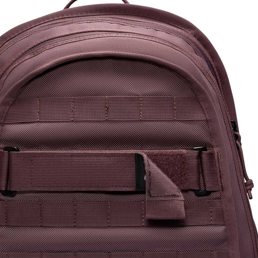 Close-up of the top section of the Tattoo Black Light Violet FD7544502 Nike SB RPM Skate Backpack, featuring mauve water-resistant fabric, a handle, zippers, and horizontal webbing straps with a Velcro patch.