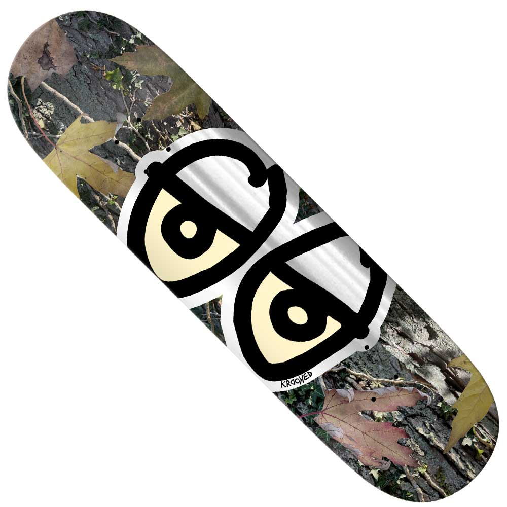 The Team Eyes Camo Foil 8.5 Krooked Skateboards Deck features a camo foil pattern of leaves and bark, accented with bold cartoon-style eyes with black outlines and cream centers in the center.