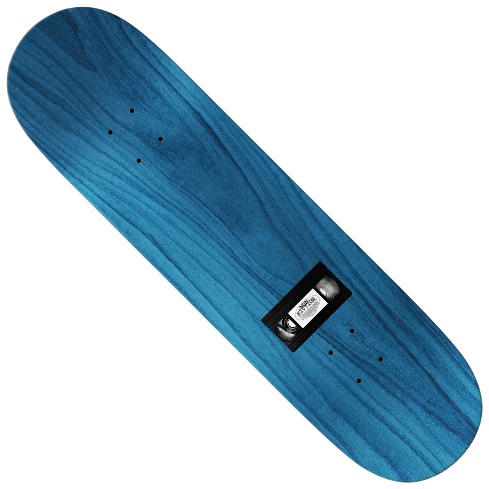 The Team Non-Fiction 8.38 Real Skateboards Deck is a blue wooden skateboard deck with a subtle wood grain pattern, shown from above. A black rectangular object with a metal part and white label is attached at the center; no wheels or trucks are included.