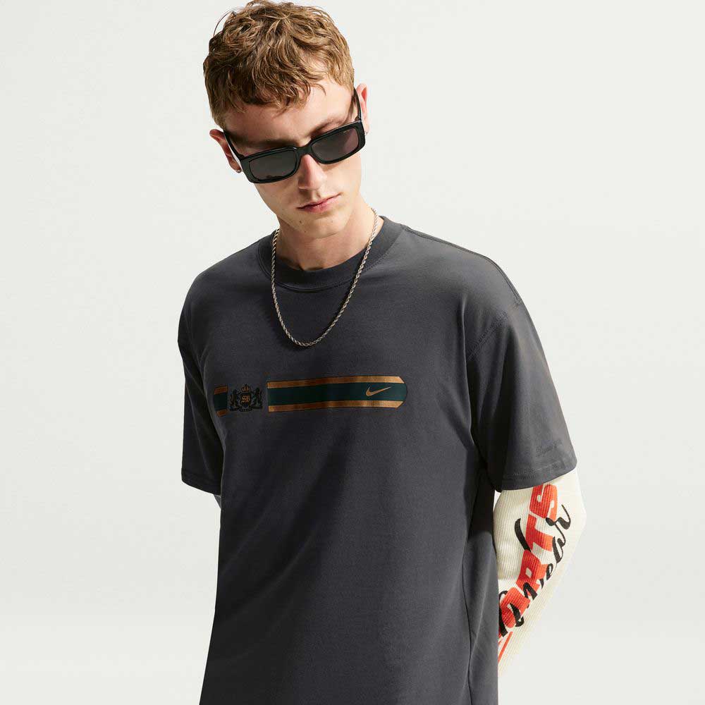 Charcoal gray short-sleeved Tee Black IW3134060 T-Shirt Nike SB Skateboarding with a horizontal chest graphic, worn over a long-sleeved shirt with red and white printed text on the sleeve.