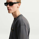 A person wearing black sunglasses and a dark gray Tee Black IW3134060 T-Shirt Nike SB Skateboarding.