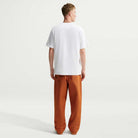 Back view of a person wearing a white Tee White IW3134100 T-Shirt Nike SB Skateboarding and loose-fitting orange trousers.