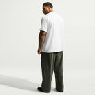 A person from behind wearing a white Nike SB Tee White IW3134100 T-Shirt Nike SB Skateboarding and baggy olive green cargo pants.