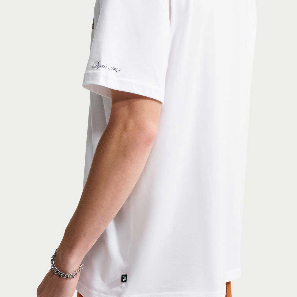 A person wearing a white Tee White IW3134100 T-Shirt Nike SB Skateboarding featuring the text Depuis 2002 on the sleeve and a small logo patch at the bottom hem.