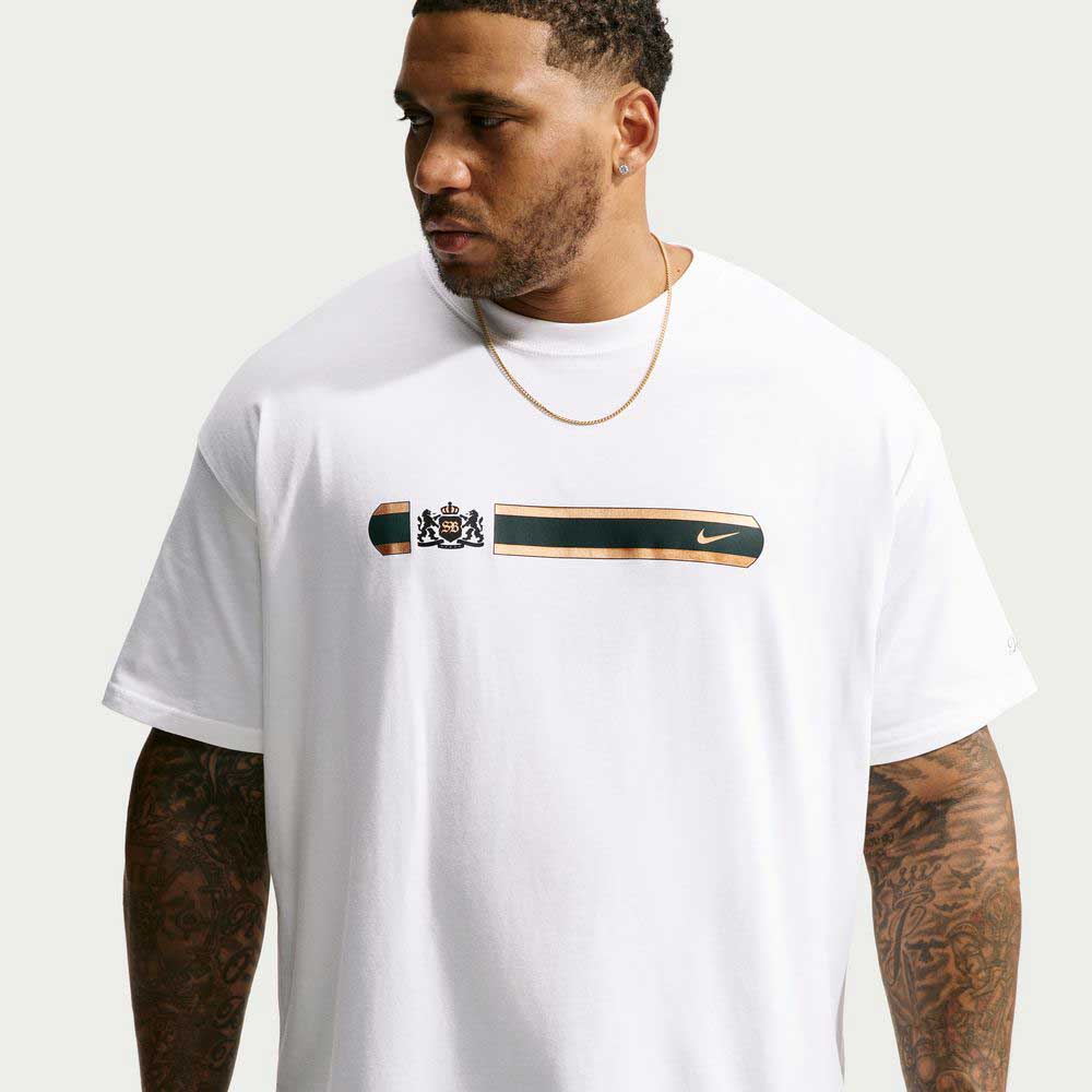 A person wearing a Nike SB Tee White IW3134100 T-Shirt, a white jersey featuring a graphic that includes a crest, a horizontal stripe, and a small swoosh logo.