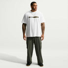 A man wearing a Tee White IW3134100 T-Shirt Nike SB Skateboarding with a horizontal graphic on the chest and olive green cargo pants.