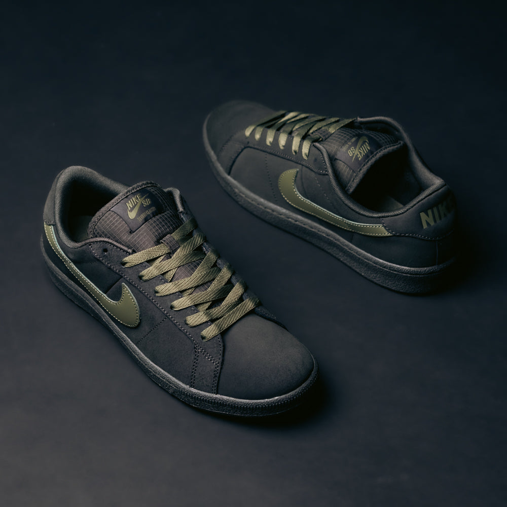 A pair of Nike SB Zoom Tennis Classic sneakers in Deep Pewter and Medium Olive suede, featuring olive green swooshes and laces, and equipped with a comfortable Solarsoft insole, displayed on a dark background.