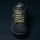 A black Nike SB Zoom Tennis Classic HF7386200 skate shoe in deep pewter and medium olive suede, featuring green laces and a green logo, displayed from the front on a dark background. Designed for comfort, it includes a Solarsoft insole for enhanced cushioning and support.