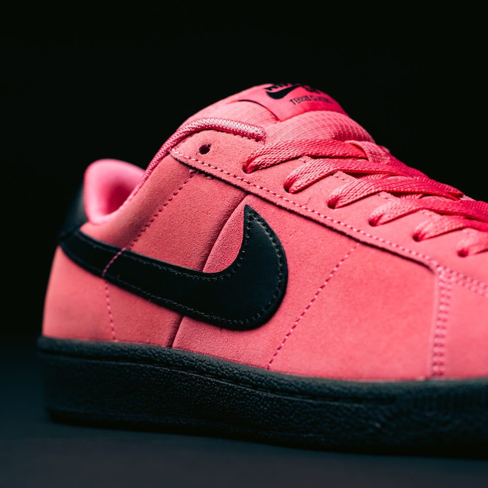 A close-up of the Nike SB Zoom Tennis Classic IO8394600 Hyper Pink Black Leather Skateboarding Shoe, featuring a bold black swoosh and black sole, with Hyper Pink laces and precise stitching detail, set against a dark background.