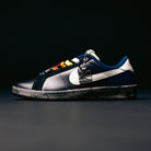 A stylish pair of Zoom Tennis Classic x Rassvet IO9846400 Blue Void Sail Nike SB leather skateboarding shoes featuring a black sole, multicolored laces, a prominent white swoosh, and a metallic tag attached to the laces, set against a dark background. Designed as versatile skate shoes, they also include a comfortable Solarsoft insole for enhanced cushioning.