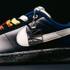 Close-up of the Zoom Tennis Classic x Rassvet IO9846400 Blue Void Sail Nike SB Leather Skateboarding Shoe, featuring a white Nike swoosh, rainbow-colored eyelets, and a metallic "RASSVET" tag hanging from the laces. This skate shoe showcases a textured black sole, dark blue upper, and is equipped with a plush Solarsoft insole for enhanced comfort.