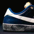 Close-up of a Nike SB Zoom Tennis Classic x Rassvet IO9846400 skateboarding shoe in Blue Void Sail, featuring a navy blue leather upper, white stripe, blue suede accents, white heel tab, and a speckled black-and-white sole against a black background. Designed for skateboarding comfort with a supportive insole.