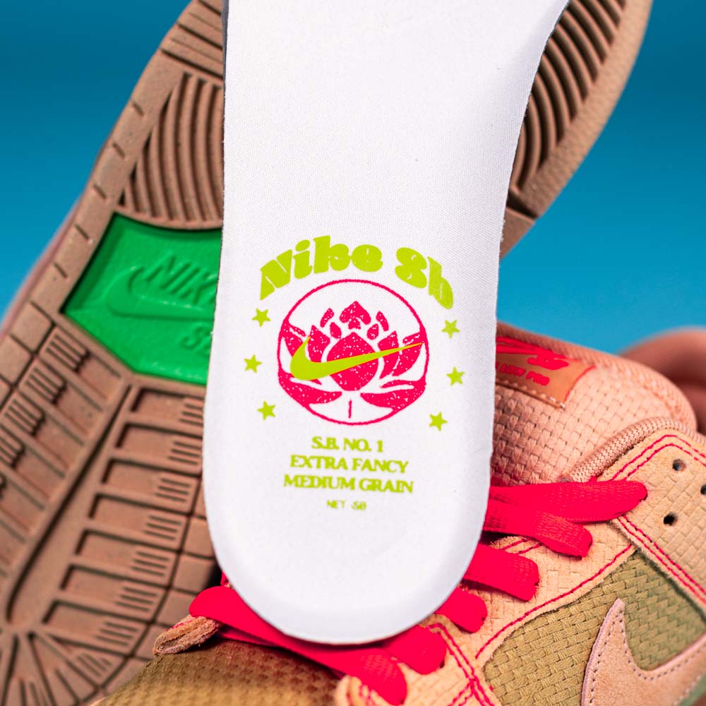 A close-up of the READ BELOW the BUTTON RAFFLE Nike SB Som Tum Dunk Low insole shows a pink lotus, yellow Nike SB logo, and “SB NO.1 EXTRA FANCY MEDIUM GRAIN” text. Pink laces and green sole; available via raffle at Southside Skatepark Skateshop.