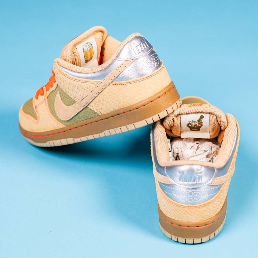 A pair of READ BELOW the BUTTON RAFFLE Nike SB Som Tum Dunk Low sneakers with beige, silver, orange laces, green accents, and Thai script on the heel is displayed. A duck graphic is shown—exclusive to a Southside Skatepark Skateshop raffle.