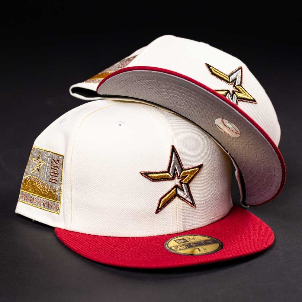 Two white and red The Final Hour New Era Hat 5950 Fitted NEW YEAR DROP caps, with gold star-shaped embroidered logos and a commemorative side patch from Whatafitted, are displayed on a black surface.