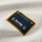 A close-up of the Thrasher Magazine x Adidas AFA Tee White KX4544 shows a rectangular embroidered patch with a gold border, Adidas logos, and blue and white "Thrasher" and "Marca Registrada" text.