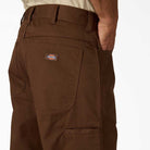 A person wearing Timber Brown Union Straight Twill Pant A88580TB Dickies Skateboarding, displaying the back pocket with the Dickies logo patch and their hand in the side pocket against a plain background.
