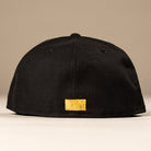 The La Morenita Black 45th Houston Astros New Era Hat 5950 Fitted by New Era is shown from the back, displaying a small gold patch near the bottom on a plain beige background—ideal for Astros fans seeking a sleek style.