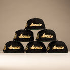 Six La Morenita Black 45th Houston Astros New Era 5950 Fitted hats with gold lettering are arranged in a pyramid on a neutral background, each featuring a colorful embroidered Mother of Guadalupe patch on the side.