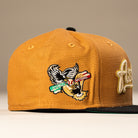 The El Gallo Canvas Bronze Black Houston Astros New Era 5950 Fitted Hat features a brown design with a black brim and an embroidered eagle holding a red, white, and green banner with gold text on the front panel. Neutral blurred background.