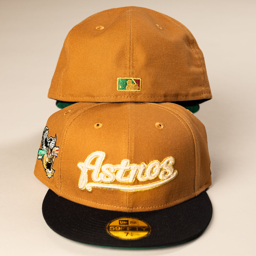 Two El Gallo Canvas Bronze Black Houston Astros New Era Hat 5950 Fitted caps are shown; the front cap features "Astros" in gold, a cartoon patch on the side, and an MLB sticker on the brim. The back cap displays the Houston Astros MLB logo.