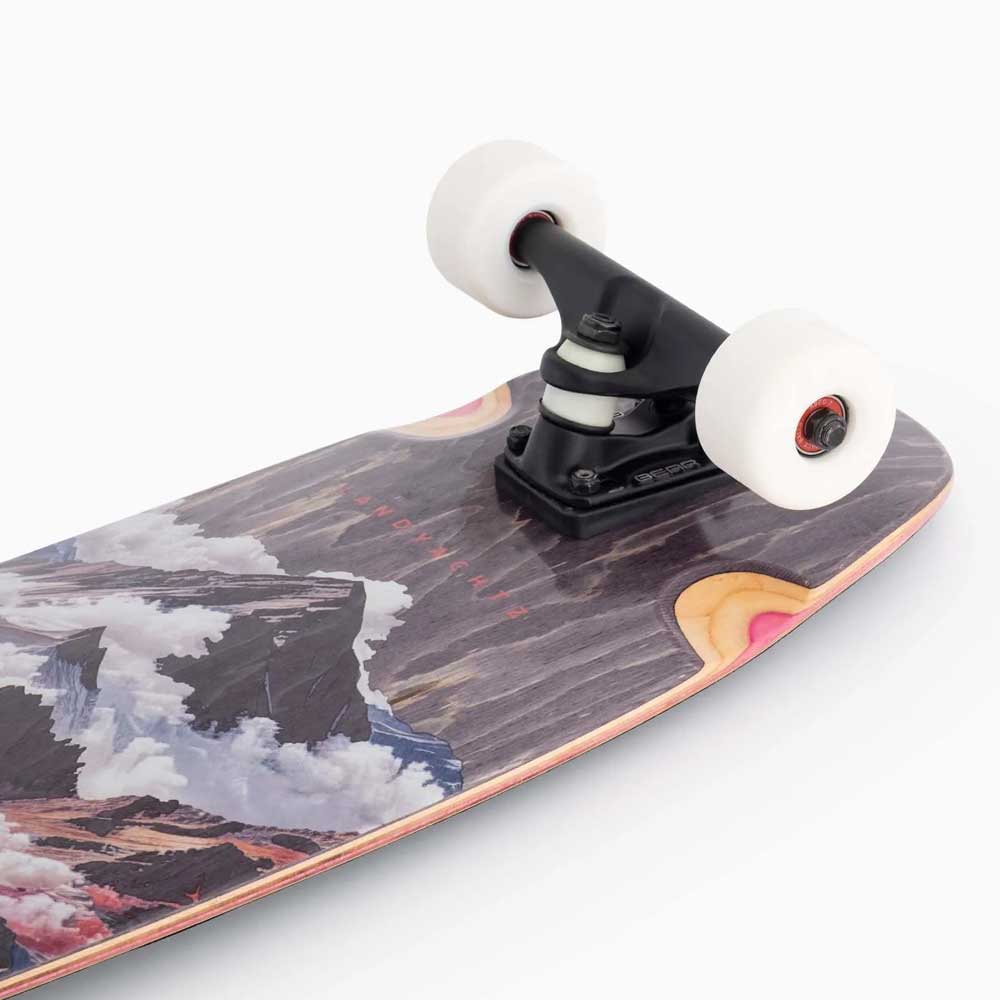 Close-up of the Tugboat Atmosphere Landyachtz Complete Skateboard’s front with white wheels, black truck, and a wooden deck showcasing a vibrant mountain landscape graphic. Ideal for urban cruising. Plain white background.