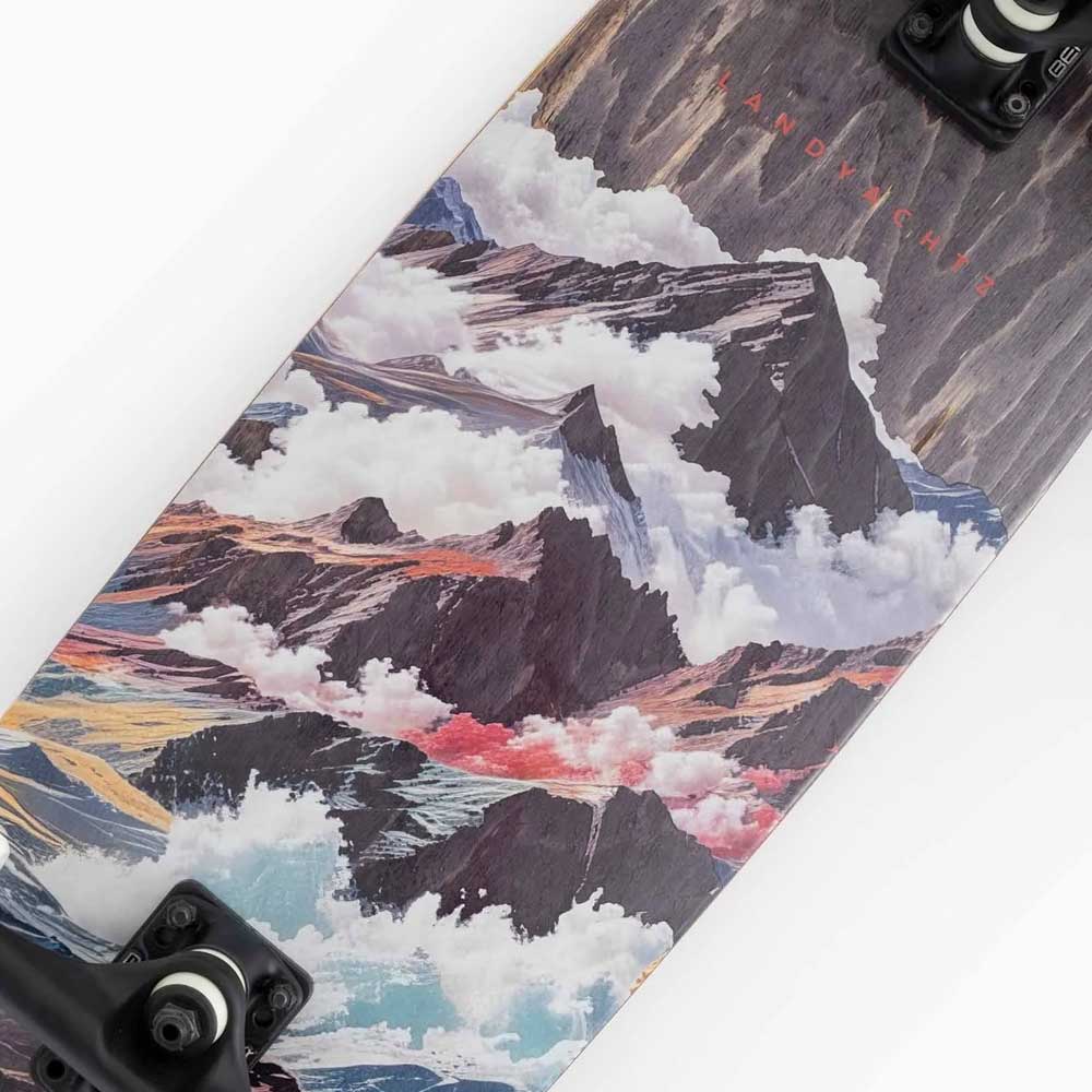 The Tugboat Atmosphere Landyachtz Complete Skateboard features a vibrant mountain landscape design with clouds, paired with black trucks and wheels—ideal for a smooth, stylish urban cruising experience.