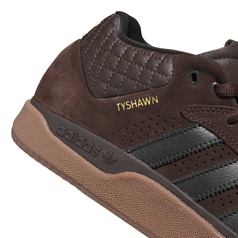 Close-up of the Tyshawn HQ4740 Brown Gum Adidas Skateboarding Shoes, featuring black stripes, premium suede with quilted textures, a gum sole, and "TYSHAWN" embroidered in gold—classic style for skateboarding.
