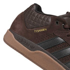 Close-up of the Tyshawn HQ4740 Brown Gum Adidas Skateboarding Shoes, featuring black stripes, premium suede with quilted textures, a gum sole, and "TYSHAWN" embroidered in gold—classic style for skateboarding.