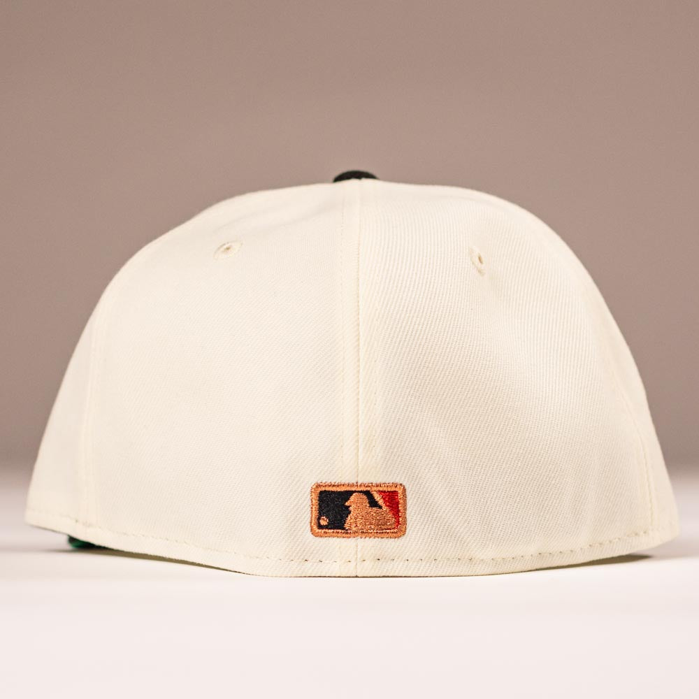 The Cougar 2.0 Houston Astros New Era Hat 5950 Fitted is shown from the back, displaying its cream color and a small embroidered MLB logo patch near the bottom edge against a softly lit plain background.