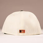 The Cougar 2.0 Houston Astros New Era Hat 5950 Fitted is shown from the back, displaying its cream color and a small embroidered MLB logo patch near the bottom edge against a softly lit plain background.