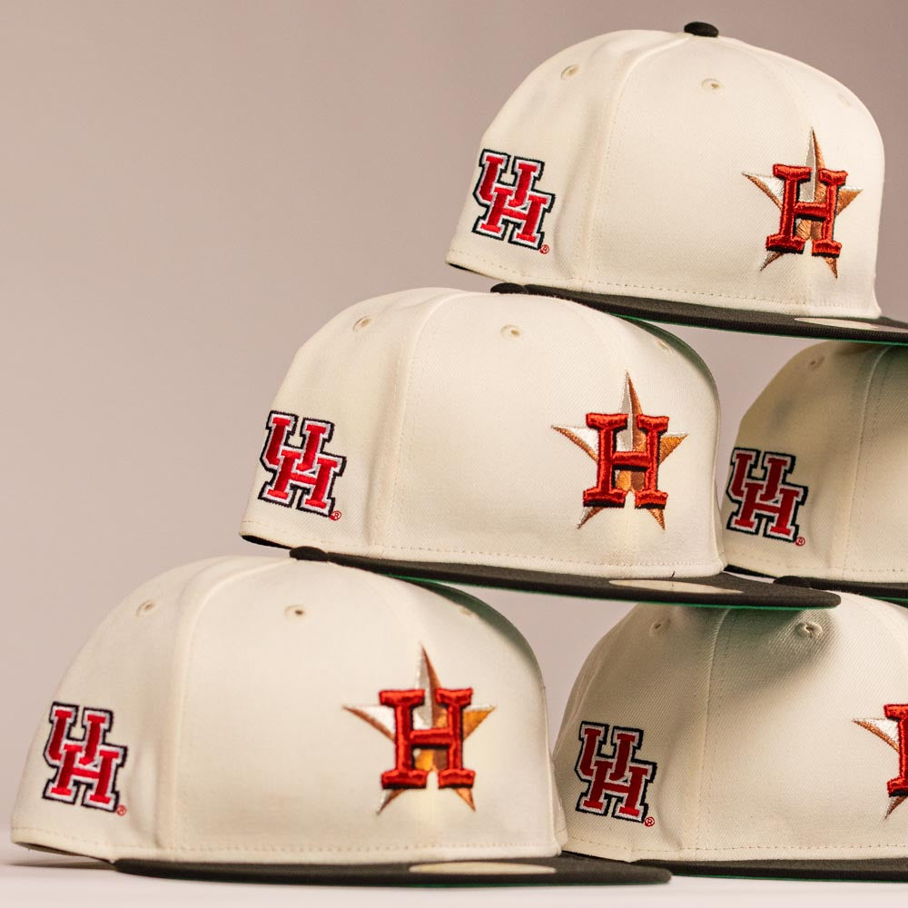 A stack of The Cougar 2.0 Houston Astros New Era Hat 5950 Fitted, with red UH and orange star H logos, representing the University of Houston and Houston Astros, is arranged against a neutral background.