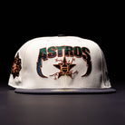 The Undaground 22WS Chrome Houston Astros New Era Hat 5950 Fitted is a white fitted cap featuring bold ASTROS text, a star logo, and decorative stitching on the front. It has a black brim, a Chrome Undaground patch detail on the side, and is displayed against a dark background.