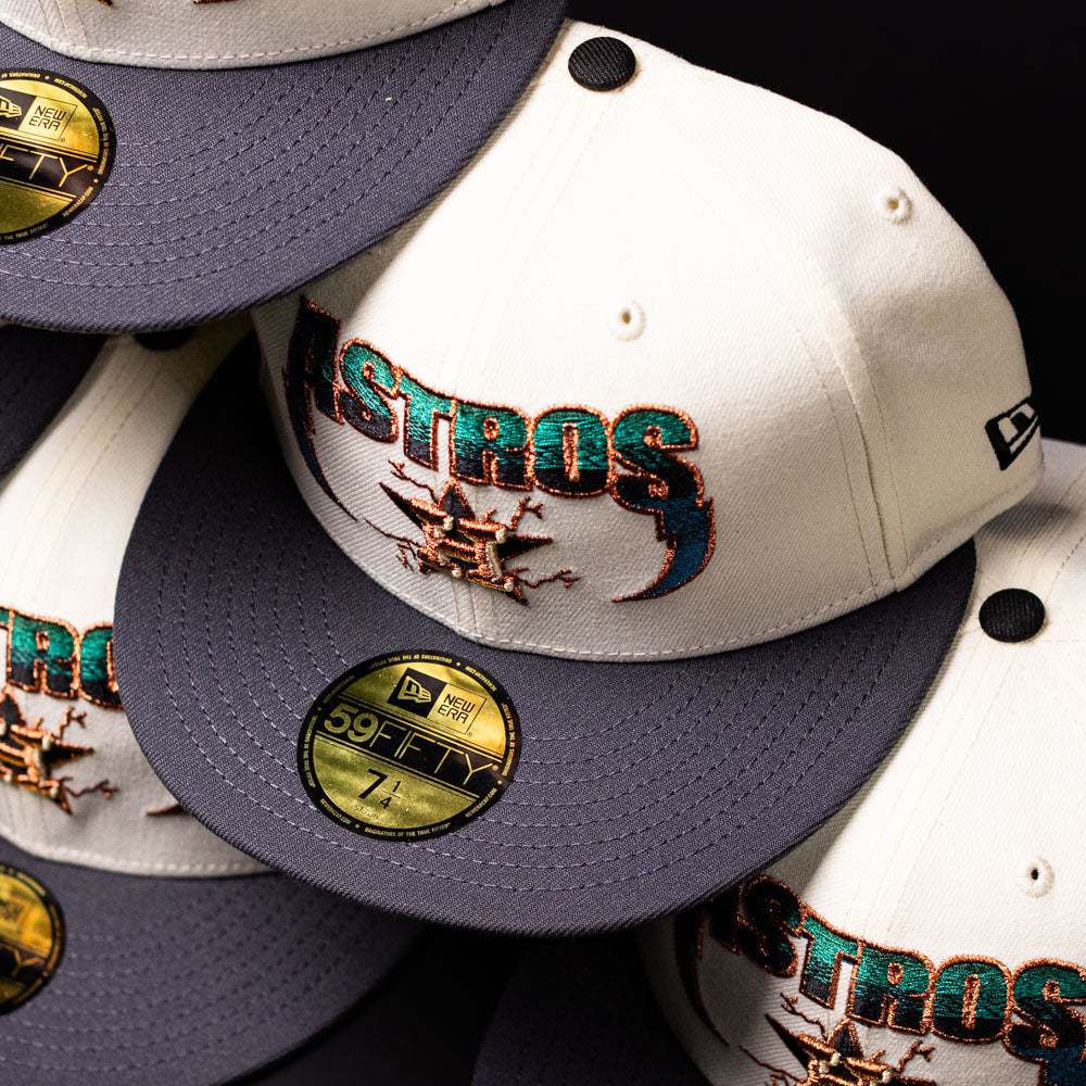 Several cream-colored Undaground 22WS Chrome Houston Astros New Era Hat 5950 Fitted caps, featuring gray brims, embroidered logos, and gold size stickers, are stacked closely together. These hats from the Chrome Undaground collection exemplify a sleek fusion of classic design and modern streetwear style.