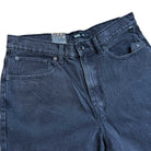 A close-up of Vans Skateboarding Skate Check 5 Loose Shorts in washed black denim (VN000C9VEMQ1) featuring visible stitching, front pockets, belt loops, a button closure, and an inner waistband brand tag.