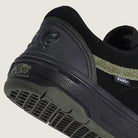 Close-up of Vans Skate Half Cab Walnut Gum VN0A5FCD77J1 suede skateboard shoes in black, featuring a textured green stripe, PopCush impact protection, WAFFLECUP sole, and "Off The Wall" heel label against a plain background. Perfect for skateboarding.