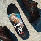 A colorful Vans PopCush insole with abstract designs and logos is displayed on rough concrete near two Vans Skate Half Cab Walnut Gum VN0A5FCD77J1 suede skateboard shoes.
